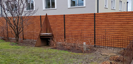Holz-Sichtschutzzaun mit waagrechten Latten und dunklen Metallpfosten entlang eines Gartens.