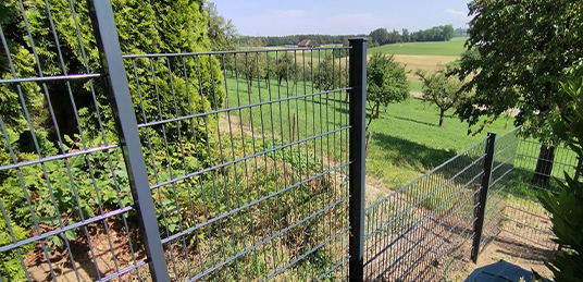 Anthrazitfarbener Doppelstabmattenzaun in abgestufter Höhe entlang eines Gartens am Hang.