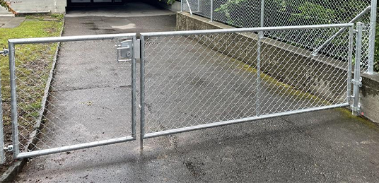 Zweiflügeliges Einfahrtstor mit Maschendrahtfüllung und unterschiedlich breiten Torflügeln vor einer Garage.