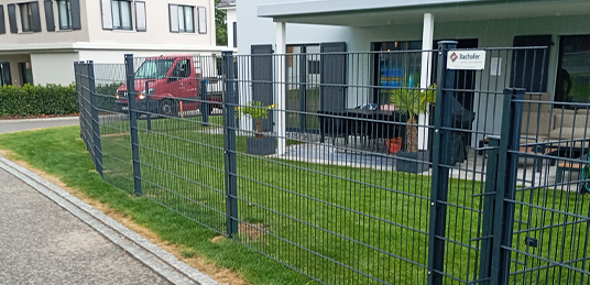 Anthrazitfarbener Doppelstabmattenzaun entlang eines Gartens mit Rasen und überdachter Terrasse.